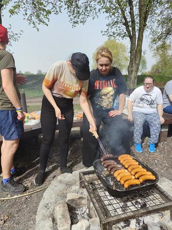 Uczestniczka i terapeutka grillujące kiełbaski na tle drzew